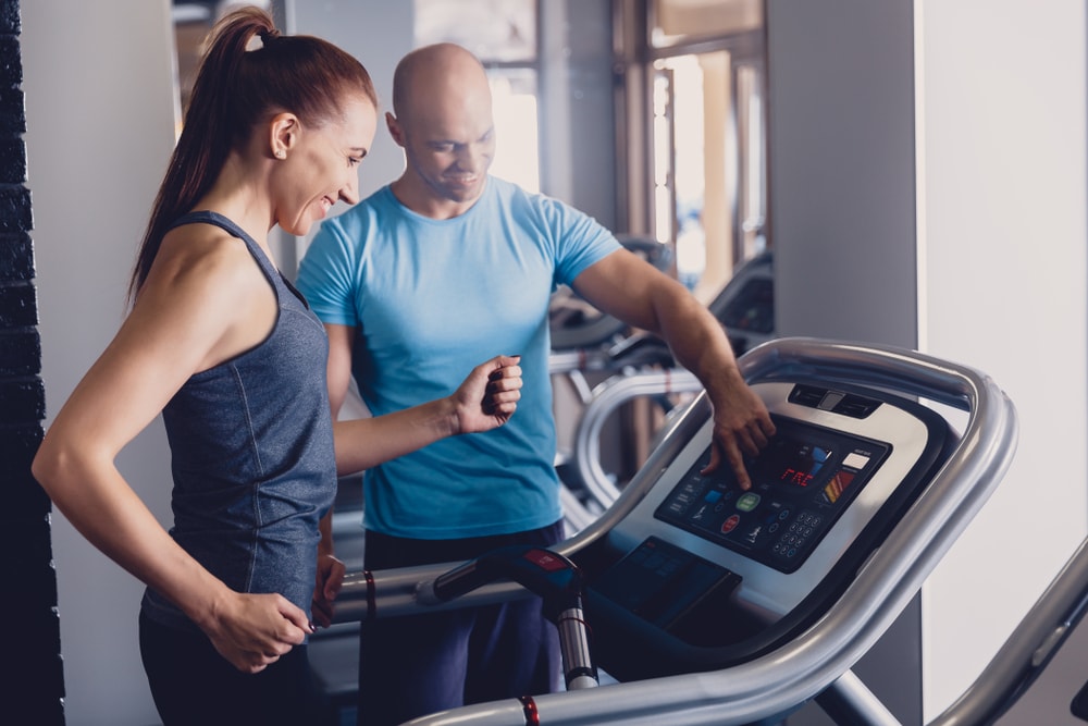 Coach helping woman running on treadmill