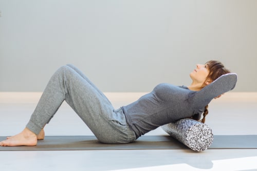 Woman foam rolling a sore back on yoga mat